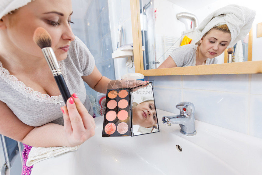 洗手间中的女人在脸颊骨上应用等式铜制器洗手间中的女人在刷子上应用等式铜制器图片