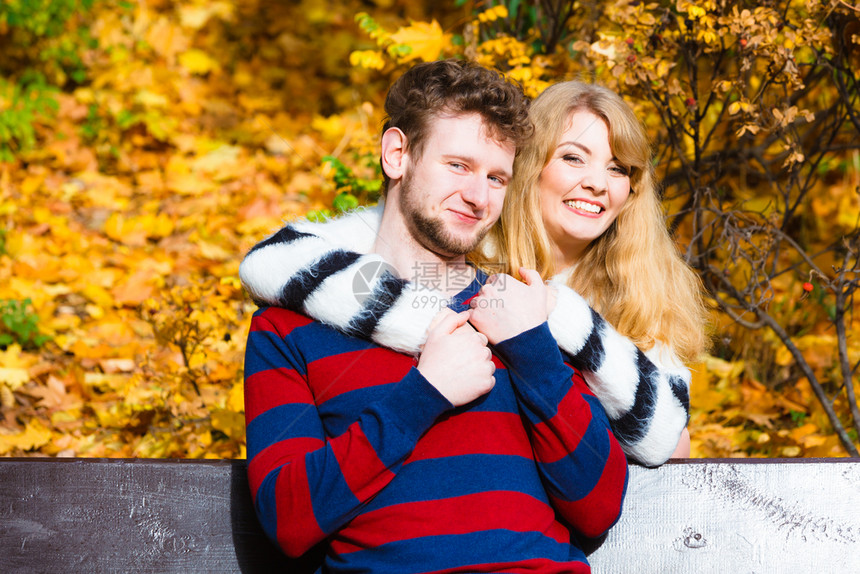 年轻夫妇坐在秋天公园的长凳上拥抱图片