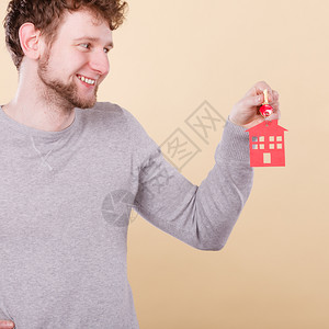 年轻有胡子的笑着脸长胡子男持有红色家庭形状的新房钥匙地产和住概念背景图片