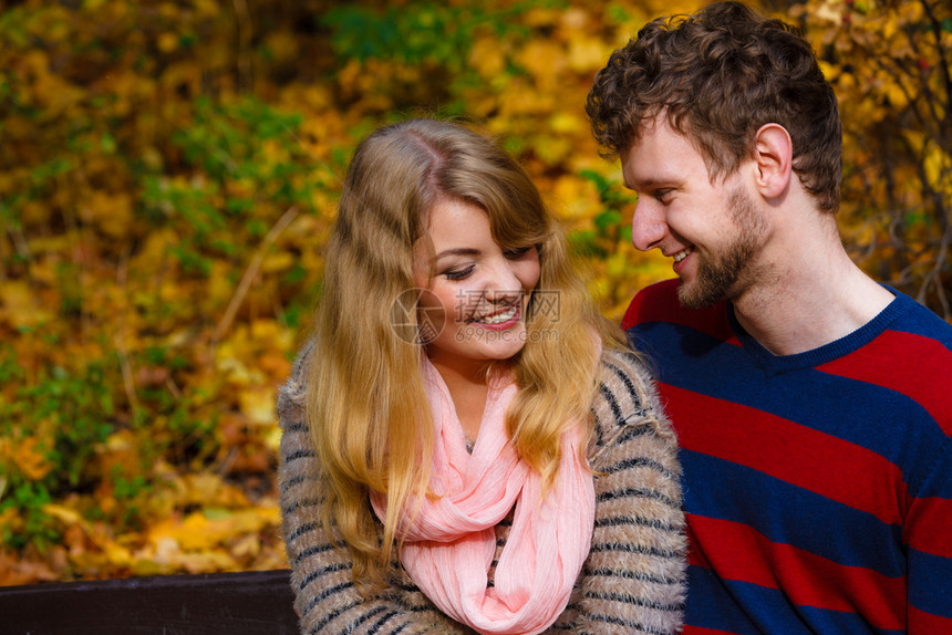 在阳光明媚的日子里年轻浪漫夫妇坐在秋天公园的长凳上拥抱在秋天公园的情侣们坐在长椅上图片