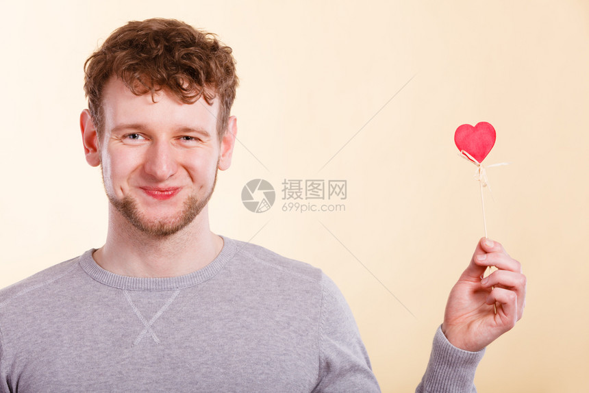 快乐的微笑年轻男人用小红心在棍子上浪漫的男人梦想着他爱情关系图片