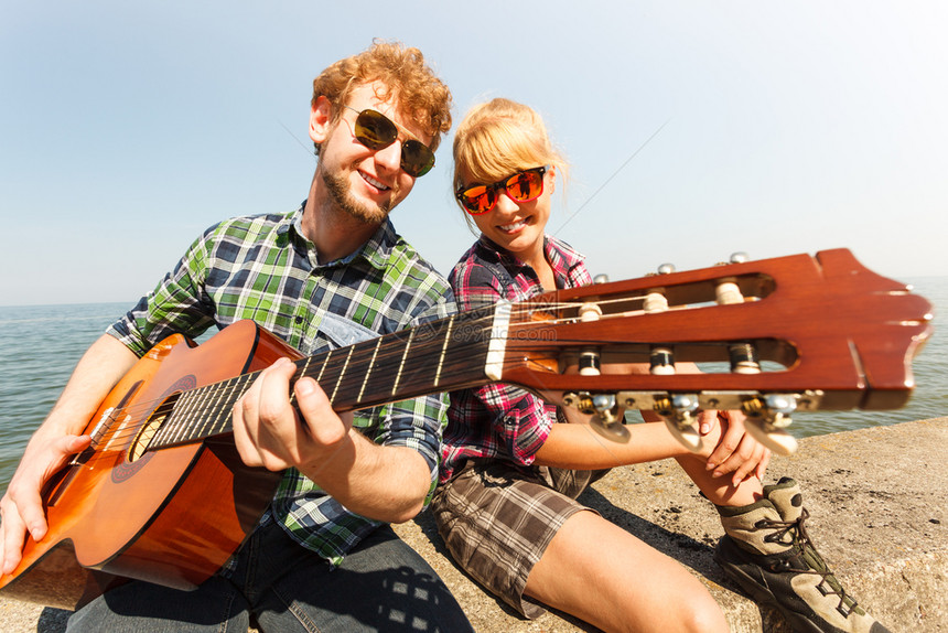 快乐的年轻男子嬉皮士在海边为女人弹吉他图片