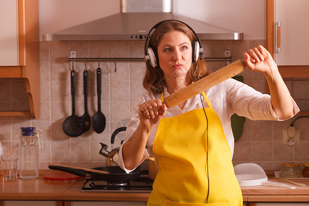 在家厨房做饭和可爱的有思想家庭主妇戴着耳机带滚动针跳舞的耳机图片