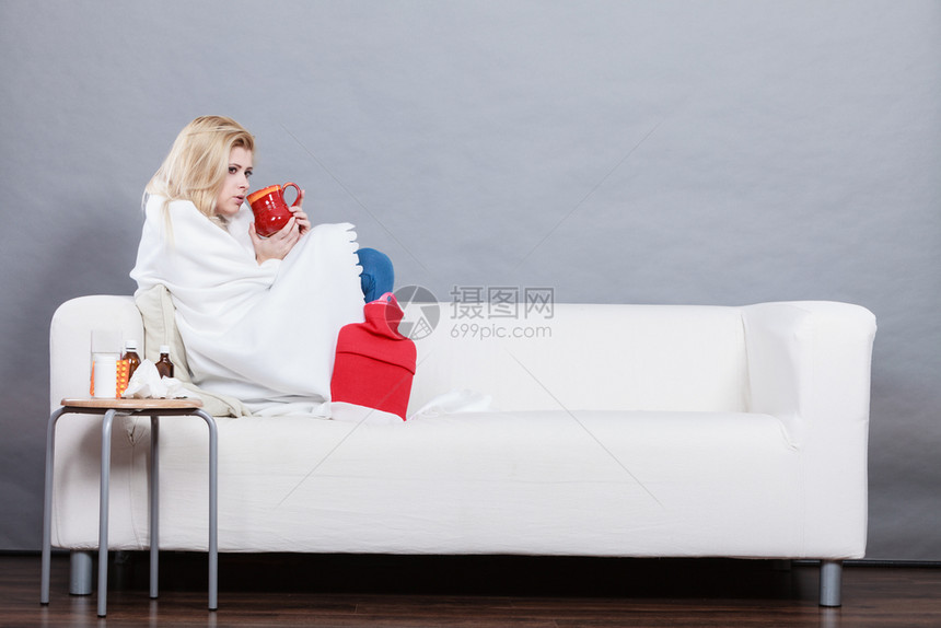 患有流感妇女拿着热饮在沙发上躺着图片