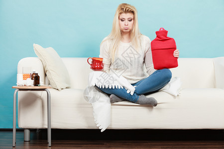 在沙发上坐用热水瓶和茶杯装子用热水瓶和茶杯装子的妇女图片