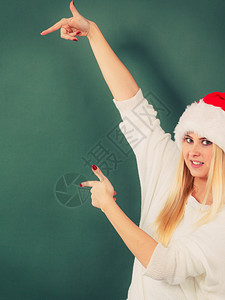 身戴圣诞老人红帽子的快乐年轻女想到圣诞礼物和节假日左指图片