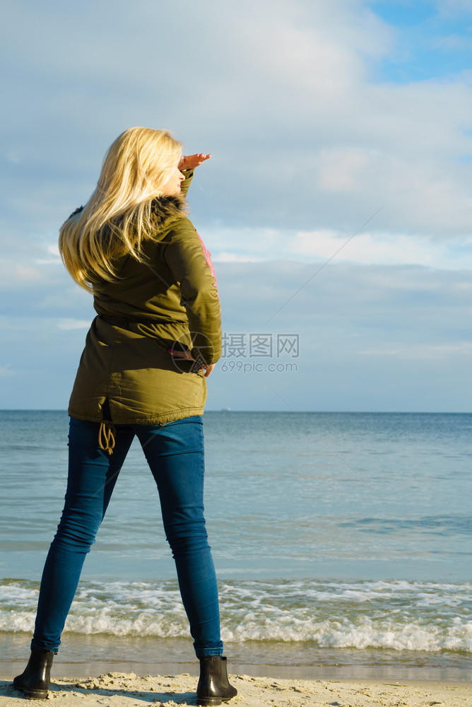 妇女穿着温暖的外套在海边沙滩阳光寒冷的天气后视海滩上的放松寒冷天气图片