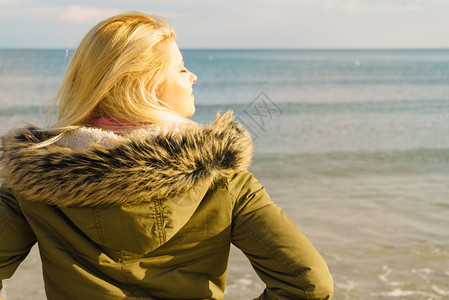 妇女穿着温暖的外套在海边沙滩阳光寒冷的天气后视海滩上的放松寒冷天气图片