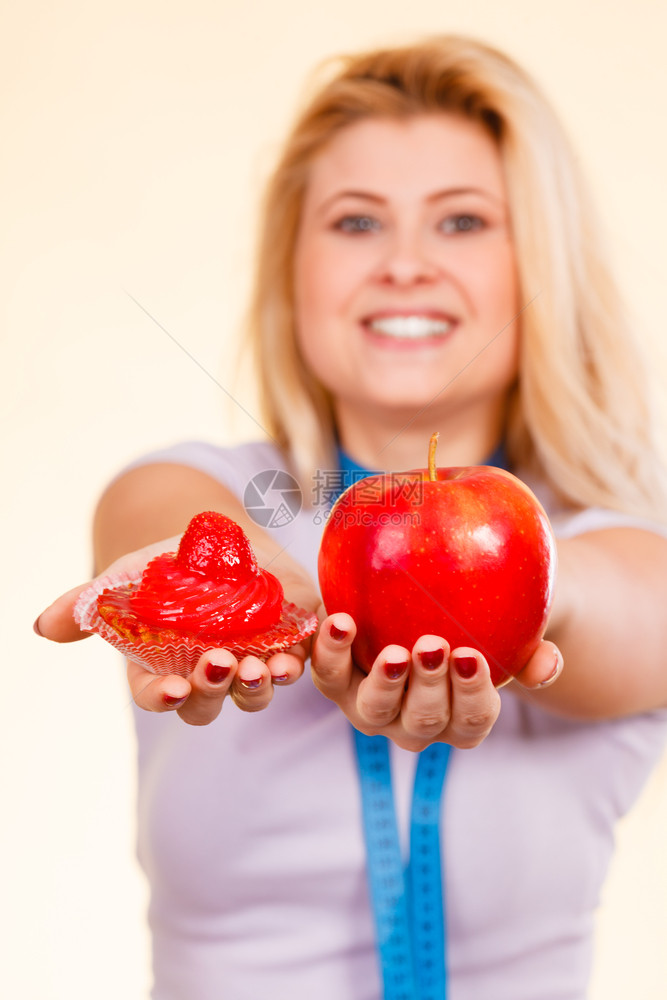 食物甜诱惑健康的选择概念妇女用测量胶带在脖子上选择苹果和甜蛋糕做决定测量胶带选择什么吃的女人图片
