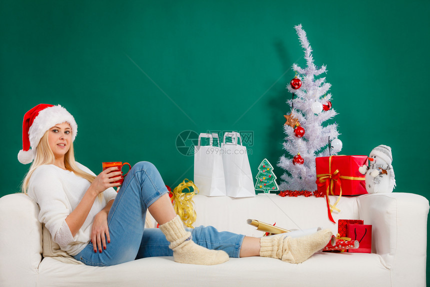 圣诞期间的放松概念穿着圣诞礼帽的金发年轻女子坐在沙发上放松享受休闲时间圣诞女子在沙发上放松图片