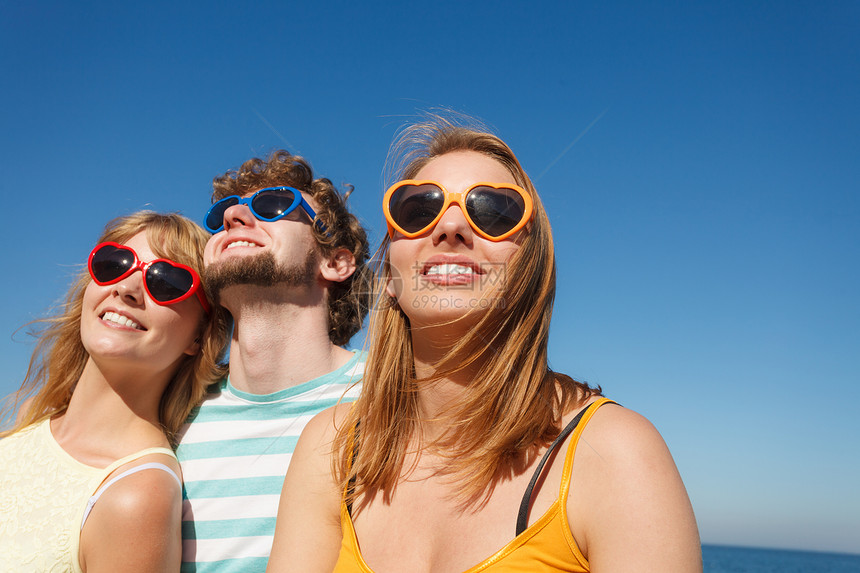 友谊快乐的暑假概念一群朋友男孩两个女坐在多彩的太阳镜里在户外与天空对着玩欢乐的心情一群朋友男孩两个女在户外玩得开心图片
