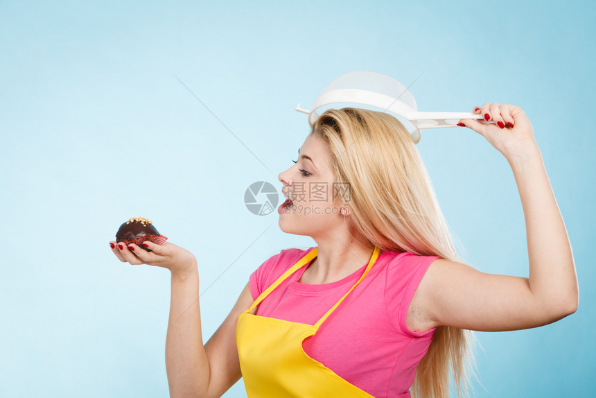 在家烘焙美味的甜点和糖果的概念一个女人拿着美味的甜巧克力蛋糕围裙戴着香炉头上戴着帽子拿着纸杯蛋糕头上戴着香炉的女人图片