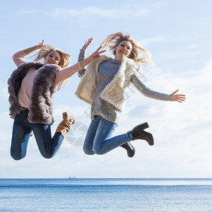 两个充满喜悦的女人与天空一起跳来去女朋友在户外玩去两位女跳起来图片