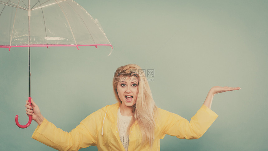 身穿黄色雨衣的金发女人拿着透明的雨伞检查天气是否下雨图片