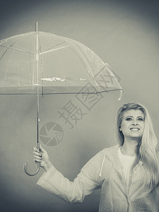 雨天时心情良好金发妇女快乐穿着雨衣拿透明伞戴图片