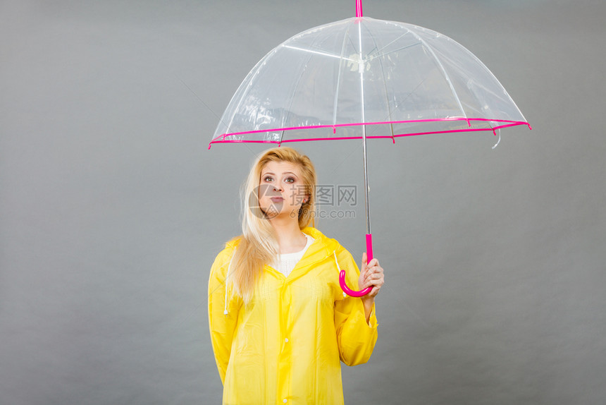 穿着黄色雨衣的无聊金发女人拿着透明的雨伞等待水图片