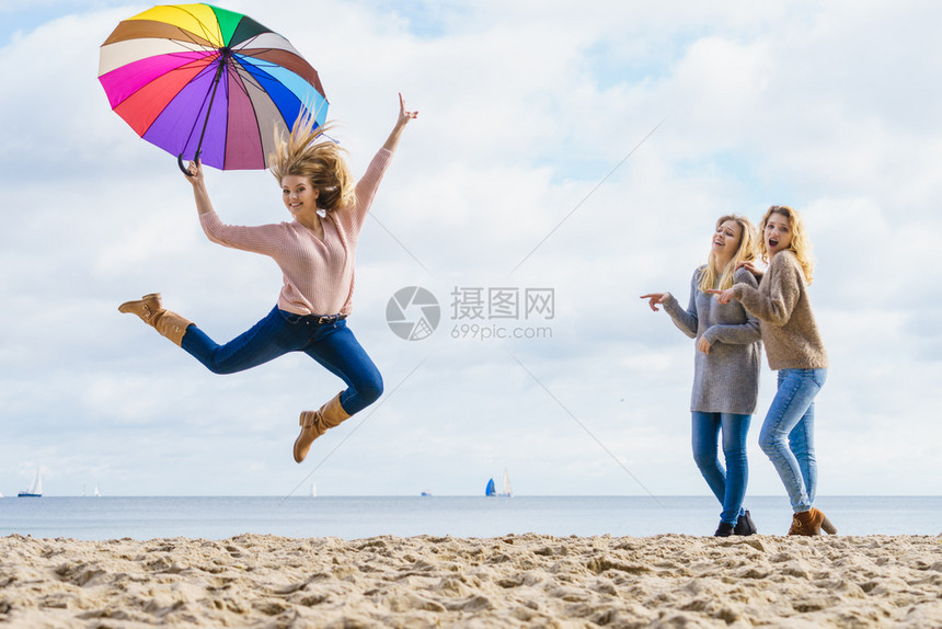 带着五颜六色雨伞的女人她的两个朋友在取笑她取笑她女人取笑跳朋友图片