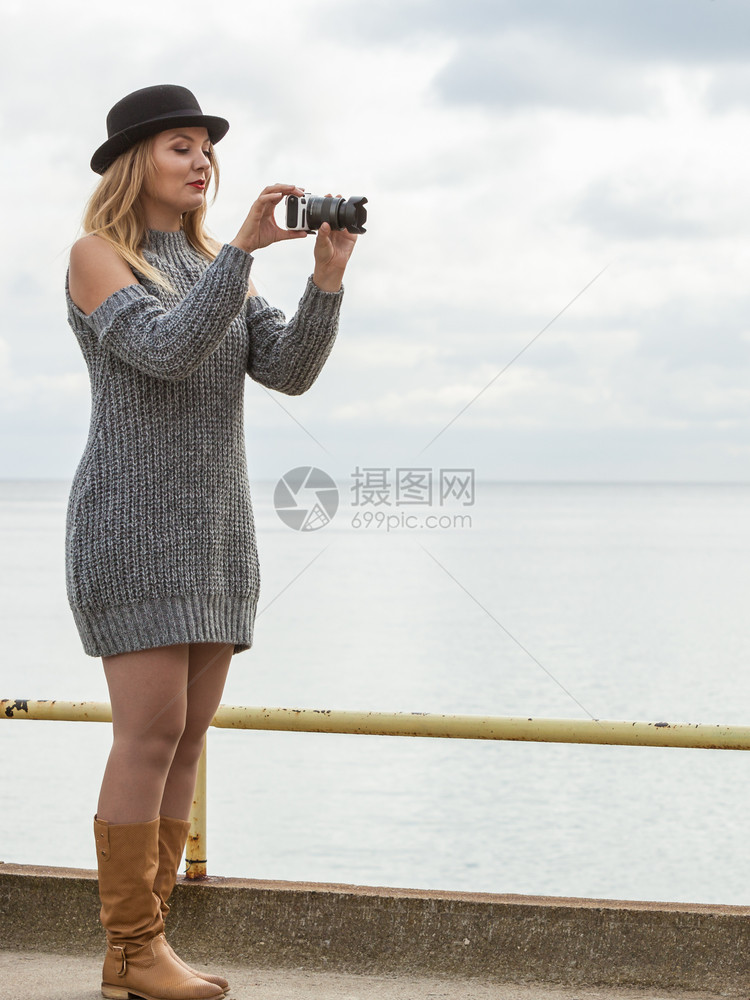 穿着黑帽子和灰色毛衣的笑女在户外拍照时使用数码相机拍照图片