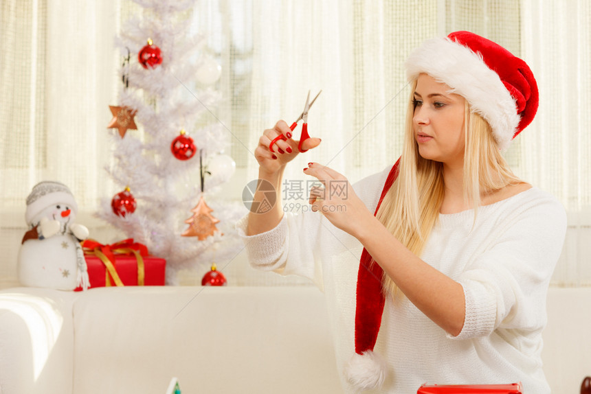 圣诞时间概念穿着圣达克萨斯帽子为圣诞节准备礼物坐在家中沙发上舒适的假日内地年轻金发女孩节快乐她们为圣诞节准备礼物图片