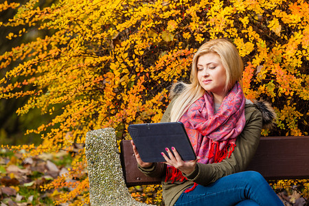 在秋天的气下妇女坐在公园的长椅上休息使用平板电脑检查社交媒体图片