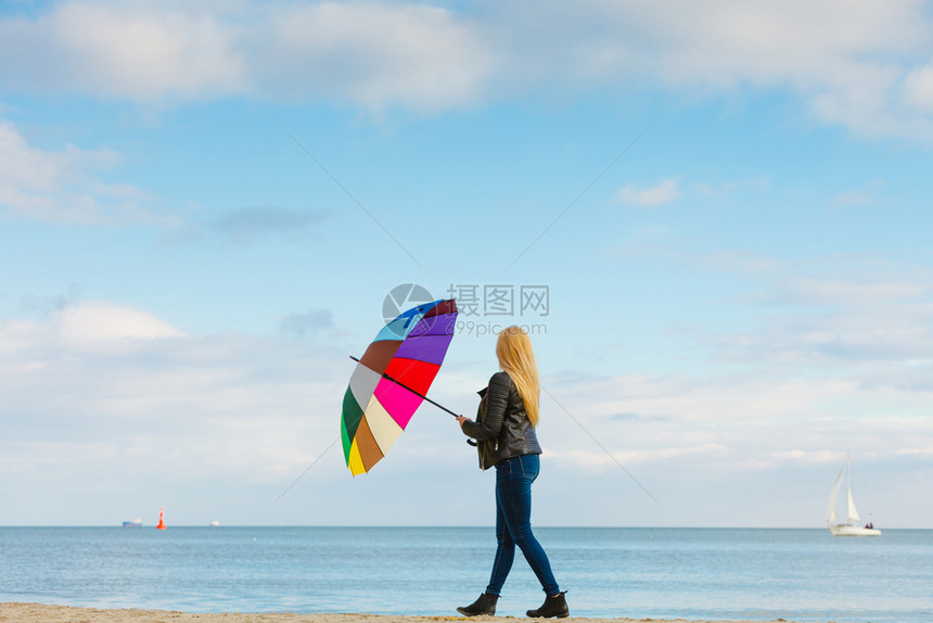 幸福享受寒冷的秋天气感受伟大的概念女人在海边的滩阳光明媚的白天和清蓝空上拿着多彩的伞女人在海滩上拿着多彩的伞图片