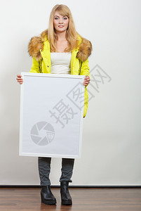穿着温暖的石灰夹克年轻女子拿着白空板横幅秋冬时装广告图片