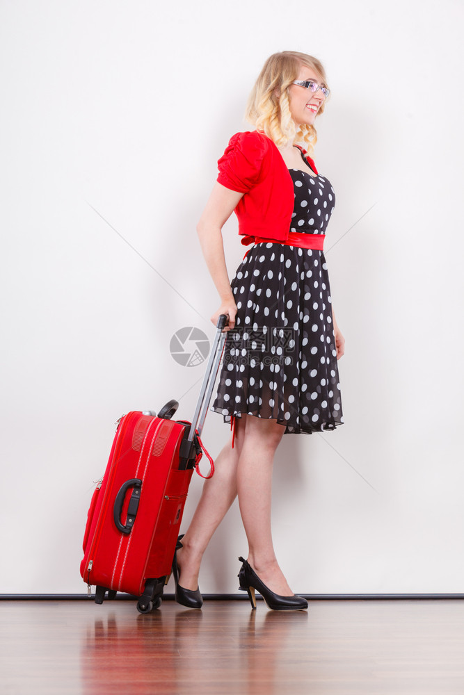 旅行度假概念身穿波尔卡圆点黑色高跟鞋准备出行的红色手提箱全身穿着波尔卡圆点黑衣服的优美年轻女子图片