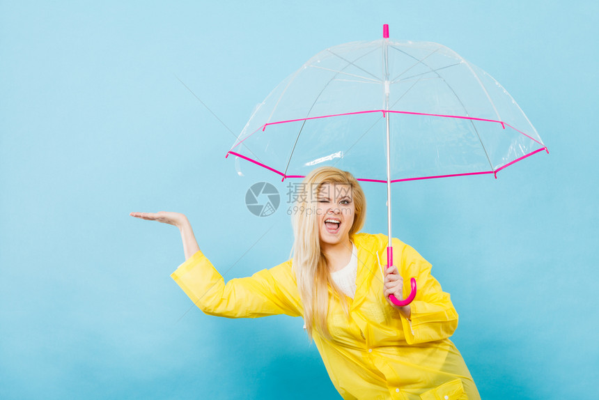 身穿黄色雨衣的金发女人拿着透明的雨伞检查天气是否下雨图片