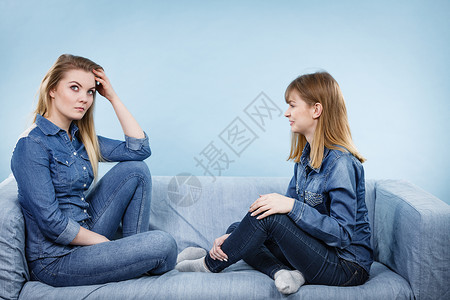 蓝色沙友谊人际关系概念两个穿着牛仔裤衬衫的严肃女朋友或姐妹在交谈论解决问题两个严肃的女朋友在沙发上交谈背景