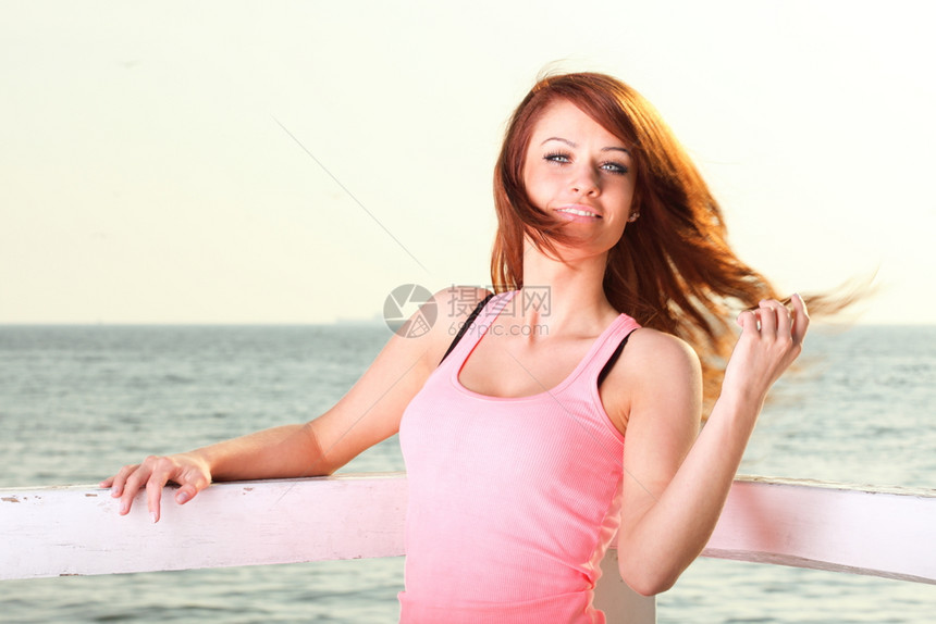 穿着头发的迷人女孩在码头冬天穿着毛发年轻女孩在海空背景图片