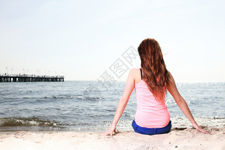 享受夏日阳光的海滩度假女人坐在沙中看着快乐的复制空间美丽的年轻模特儿图片