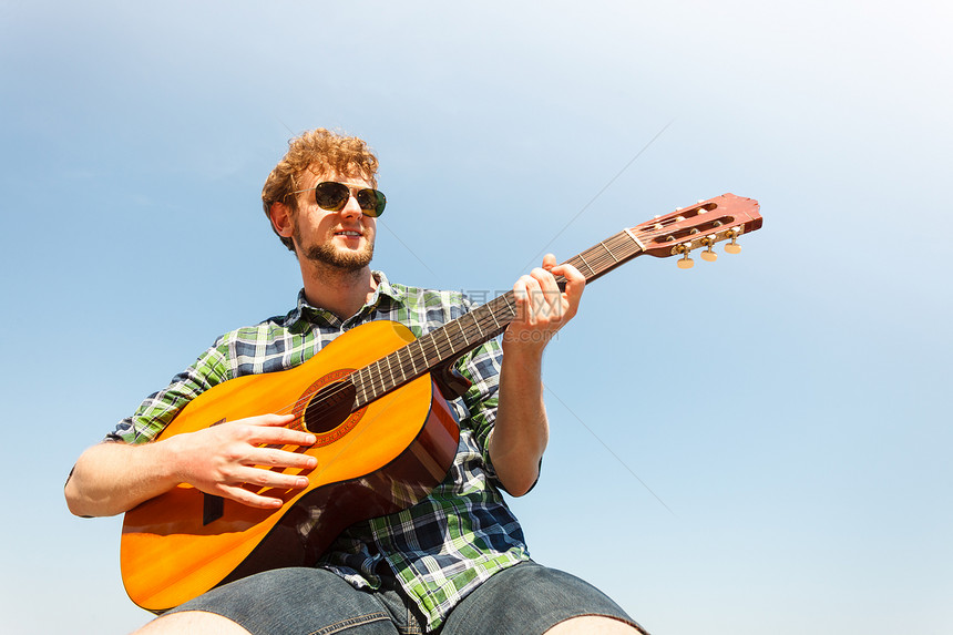 年轻嬉皮士弹吉他戴太阳镜的帅哥在暑假放松图片