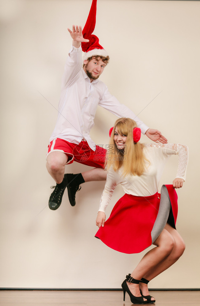 快乐的情侣跳舞和在工作室穿着圣达克萨斯帽子的漂亮女人和帅哥玩得开心圣诞节快乐的情侣跳舞和跃图片