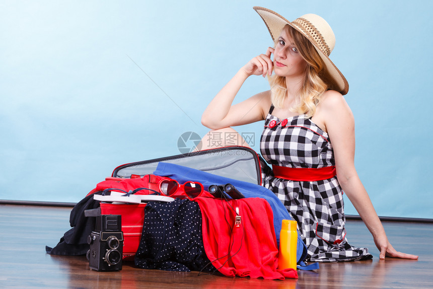 年轻女士坐在地板上拿着手提箱满的东西准备在暑假蓝色的年轻女士包装手提箱图片