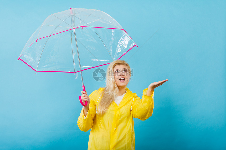 身穿黄色雨衣的金发女人拿着透明的雨伞检查天气是否下雨图片