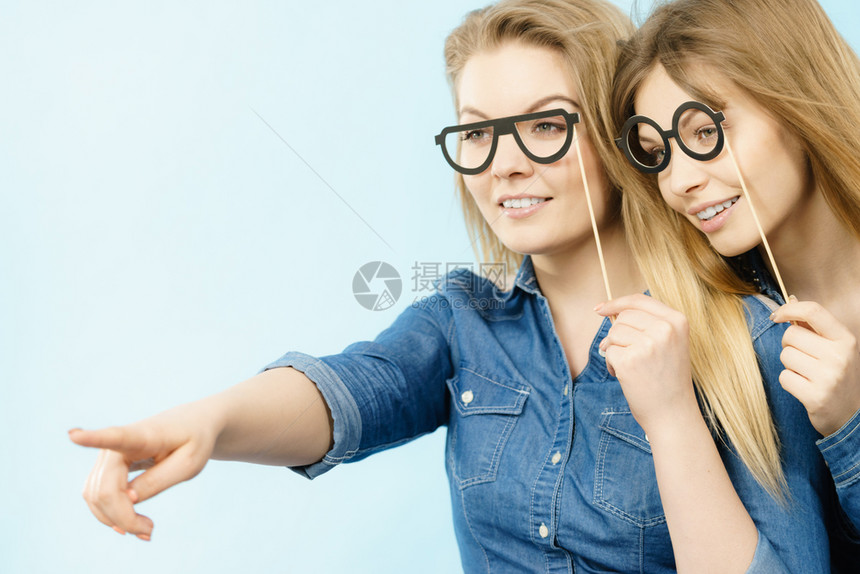 友谊人际关系概念两个穿着牛仔裤衬衫的快乐女朋友或姐妹在某个地方指着图片