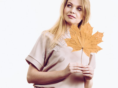 时尚的秋天长发金女孩手握着秋天干棕褐色绿叶秋天季节和预测概念图片