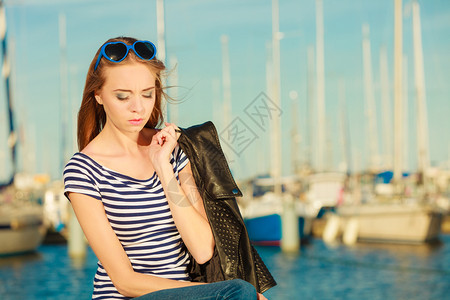 时装金发女孩蓝色心型太阳眼镜在码头对港口的游艇背景图片