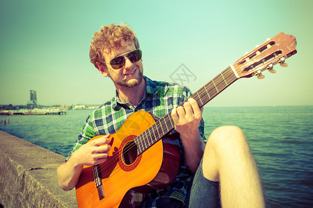 快乐的年轻人在海边弹吉他戴墨镜的帅哥放暑假放松年轻人在海边弹吉他图片