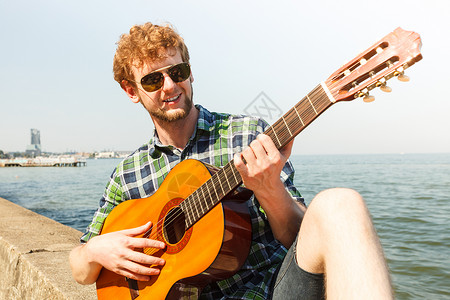 快乐的年轻人在海边弹吉他戴墨镜的帅哥放暑假放松年轻人在海边弹吉他图片