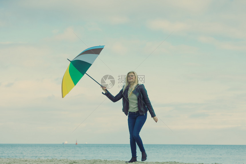 幸福享受寒冷的秋天气感受伟大的概念女人在海边的滩阳光明媚的白天和清蓝空上拿着多彩的伞女人在海滩上拿着多彩的伞图片