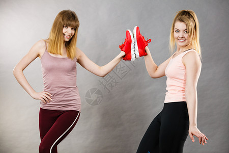 两个快乐的微笑体育女运动员展示鞋教练红舒适的合锻炼和训练图片