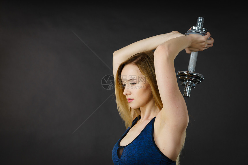 健壮的女士举起哑铃重量合适的女孩有魅力金发模特儿正在锻炼肌肉健身和美在黑暗灰色的侧面看合适的女人举起哑铃重量图片