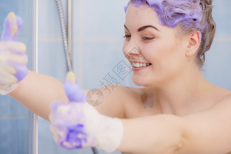 在金发上涂紫色墨粉洗发水时戴乳胶保护手套的妇女背景图片