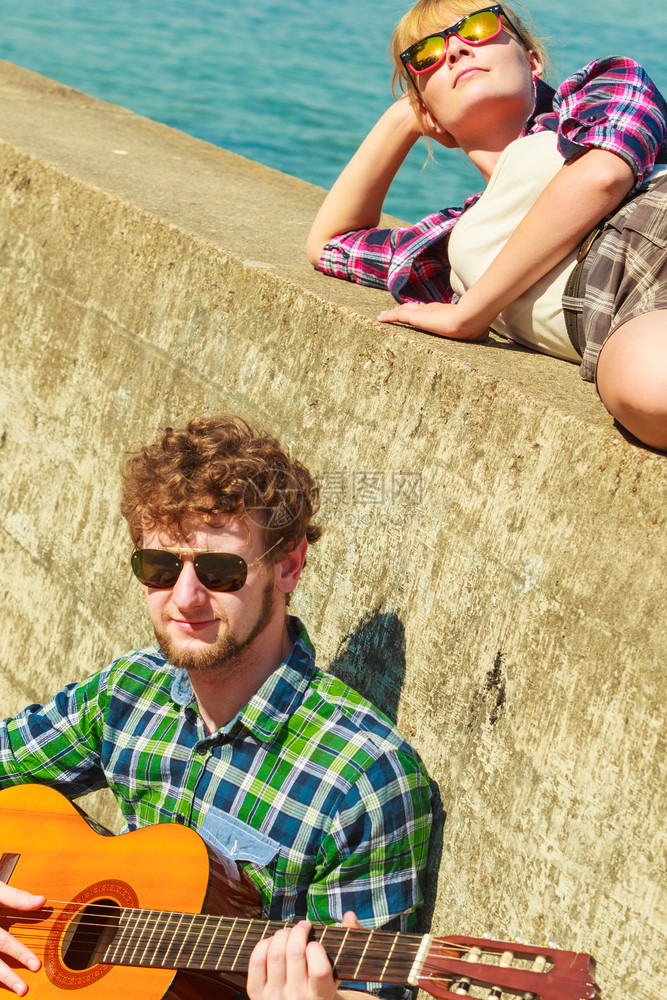 年轻男人在海边的户外和女友玩吉他约会情侣图片