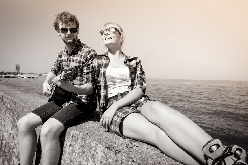 快乐的年轻男子嬉皮士在海边为女人弹吉他图片