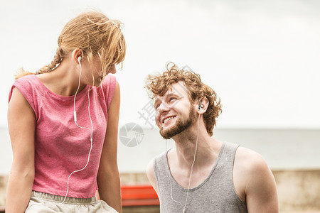 有耳机的妇女和男子在户外听音乐年轻夫妇在健身锻炼休息时放松健康的生活方式男人和女在听音乐时放松背景图片