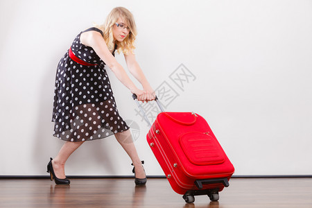 穿着Polka点黑裙子的优雅青年女拉着红色大旅行袋拉着红色大旅行袋的妇女拉着红色大旅行袋背景图片