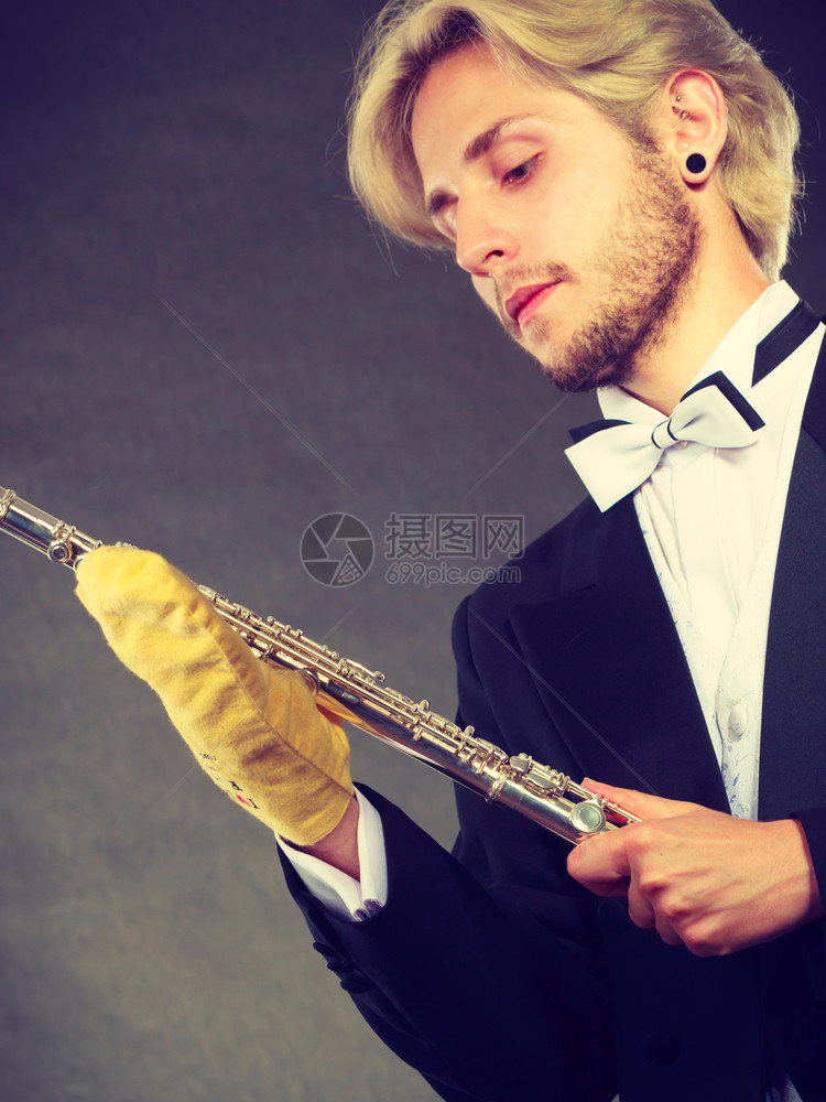 古典音乐激情和业余爱好概念穿着优美服装的音乐家金发年轻男子用黄色手帕清洗长笛深底背景拍摄工作室穿着优美服装的音乐家清洁长笛图片
