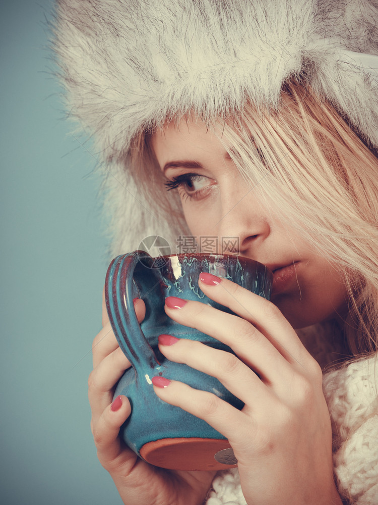 时装概念冬的金发女人喝杯茶热饮蓝背景黄发女人冬的金毛帽子喝酒图片